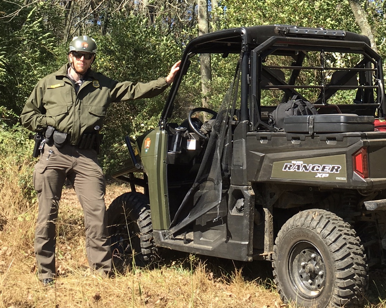 Law Enforcement Ranger leans on an ATV in the woods