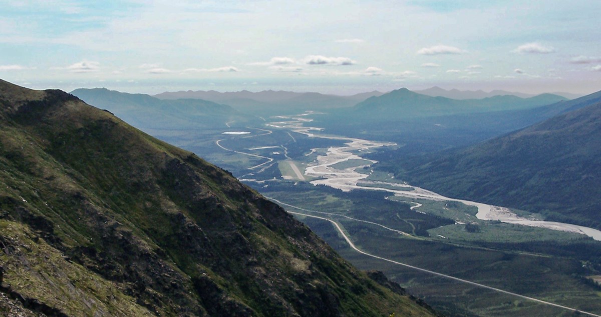 View from mountain showing broad valley below with a large river, gravel road, air strip visible in distance