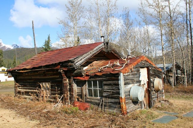 View of old and weathered two room log cabin with rusting roof