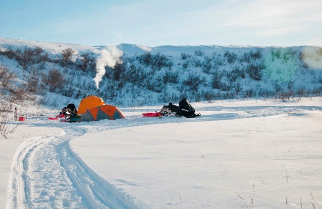 Smoke rises from the stack of an arctic oven tent on the snowy arctic tundra