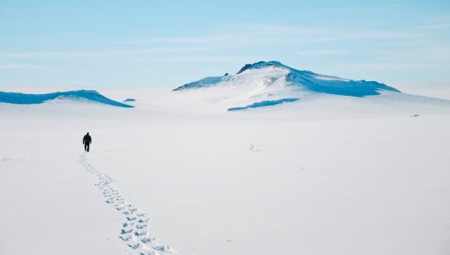 A lone snowshoer in a vast snow-covered arctic tundra landscape with mountains in background