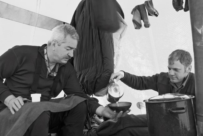 A ranger pours hot water for another ranger in a tent