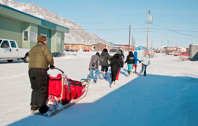 Anaktuvuk Pass kids pull a dogsled on the snowy roads through town