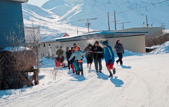 Anaktuvuk Pass kids pull a dogsled on the snowy roads through town