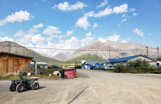 A street view of Anaktuvuk Pass, Alaska, showing homes, an ATV, and the Brooks Range mountains