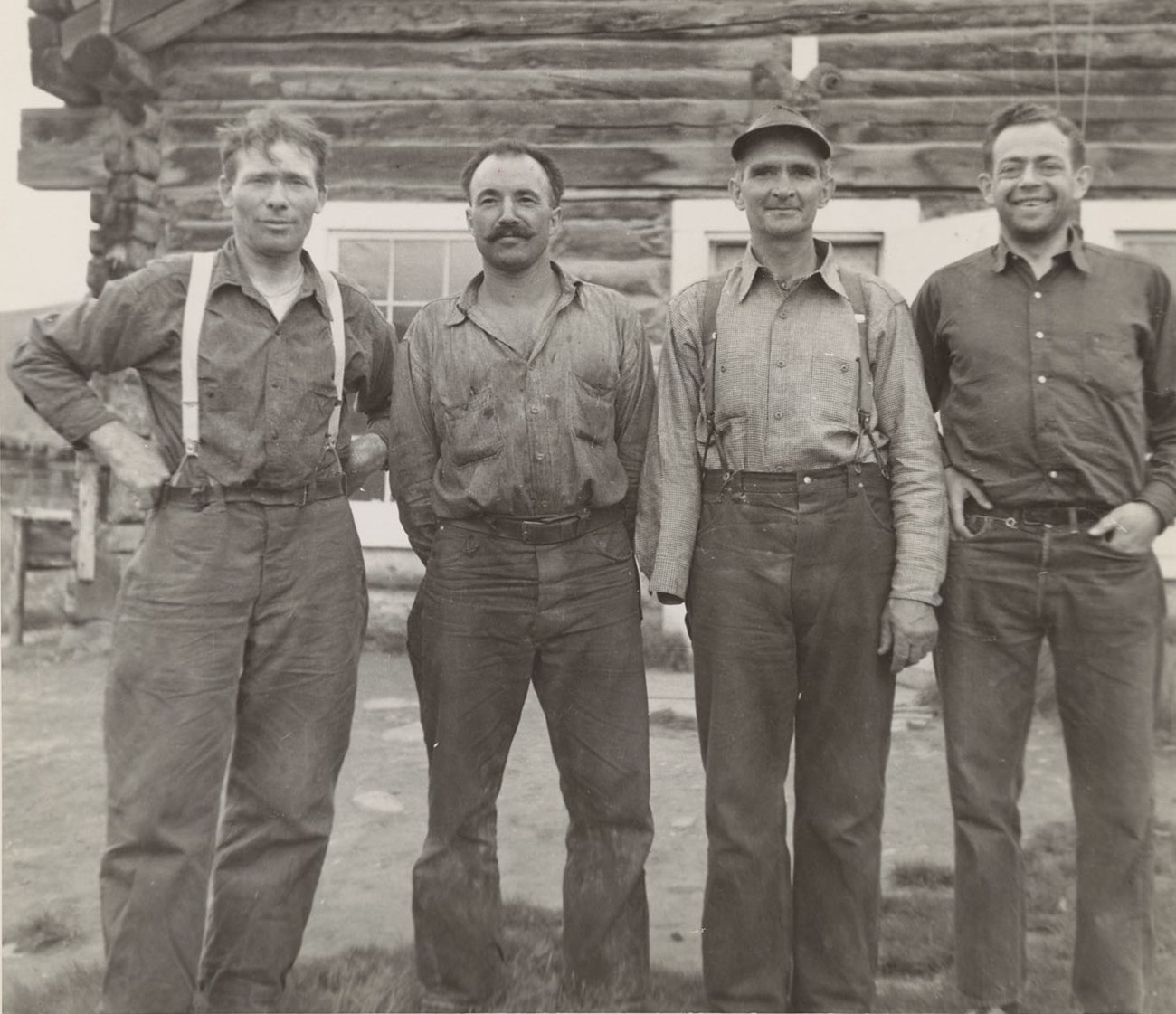 Four men stand in front of a log cabin