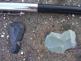 Two pre-historic worked points, one dark and one light with a pen for scale.