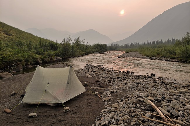 Tent on a riverside gravel bar under a smoky evening sky