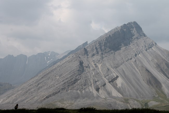 Large tilted mountain with may layers and person standing in the foreground
