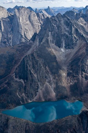 The grey granite spires of the Arrigetch Peaks frame a turquoise blue cirque lake.
