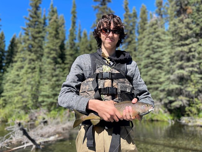 man with brown hair and sunglasses holds a fish in his hands