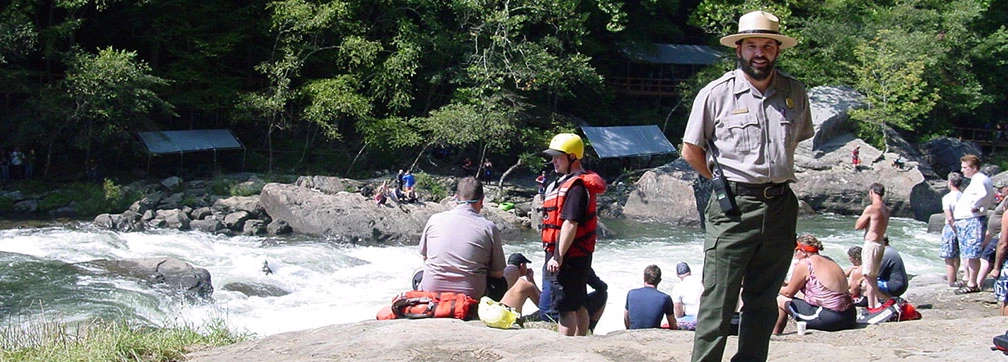 ranger standing by river with rafters ranger standing by river with rafters