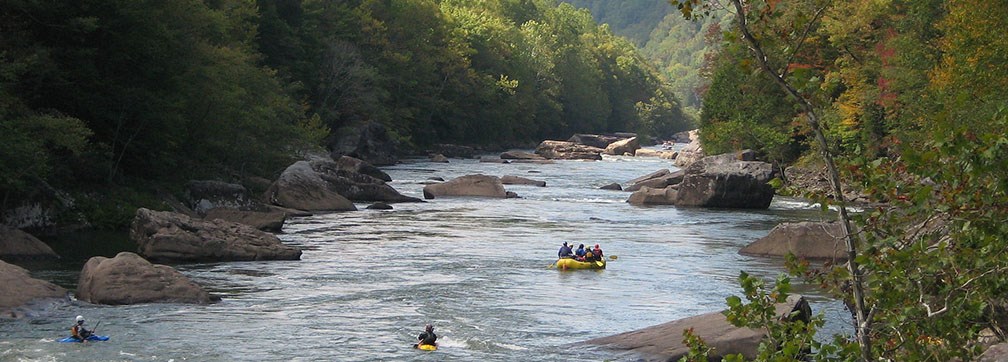 a raft and two kayakers on a boulder strewn river