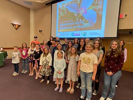 a group of kids pose in front of screen with wildflower a group of kids pose in front of screen with wildflower