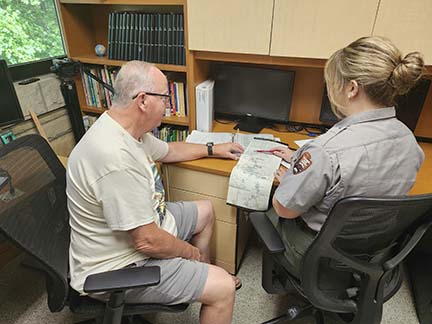 park ranger at a desk looking at a map with an older man