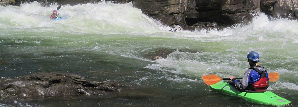 Kayaker watching a second kayaker navigate through rapids
