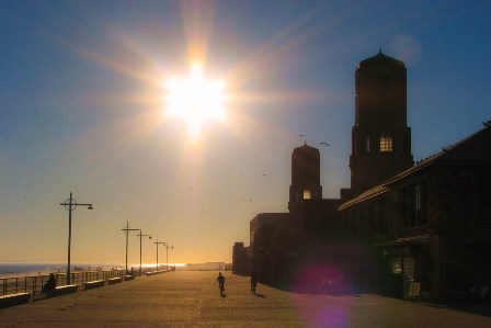 two boys riding down the Riis Park boardwalk in front of the historic bathhouse