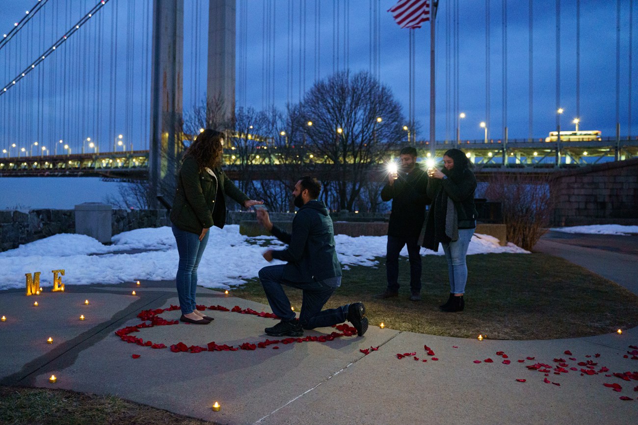 Man on knee in front of woman with rose petals