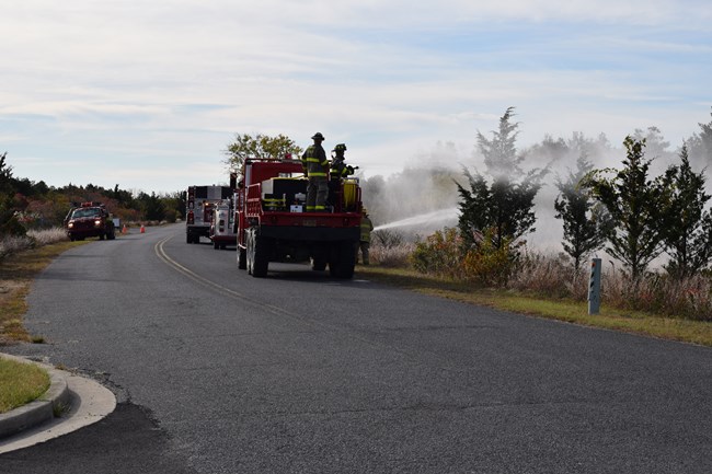 Gateway and NJ Forest Fire Cohost Interagency WUI Drill Photo showing various fire trucks hosing down trees in an interagency fire drill.