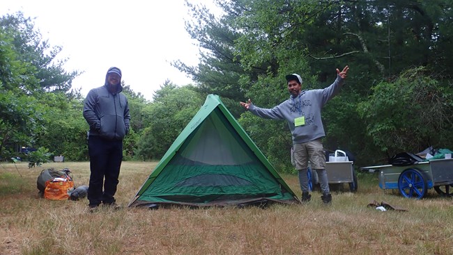 Two adult individuals pose next to a tent at Ecology Village.