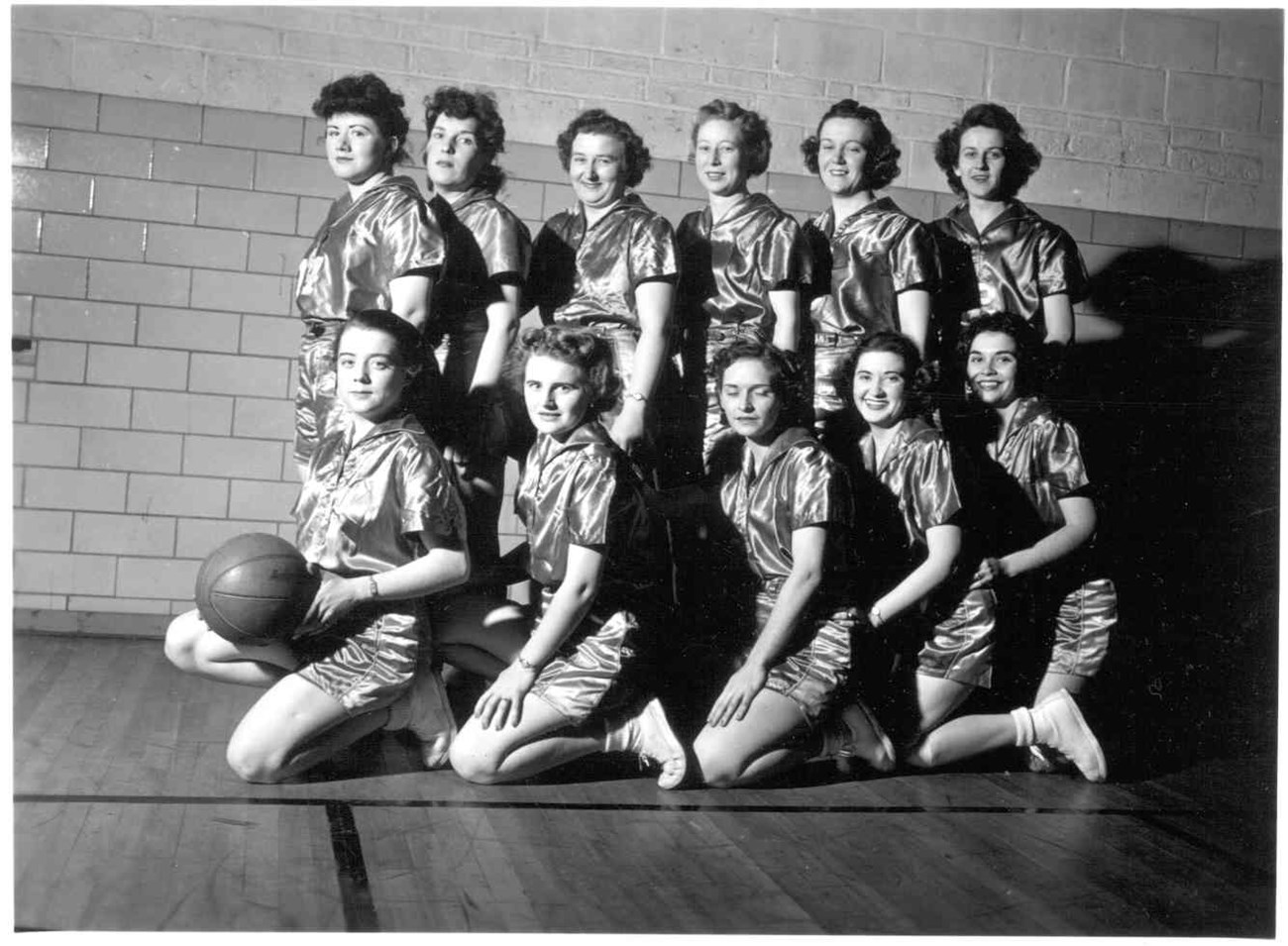 a dozen women pose in a gym holding a basketball