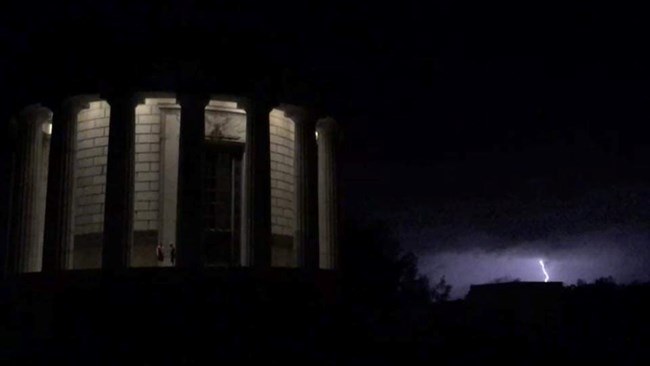 memorial on left two people standing under the lite rotunda with lightning on the right