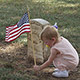 toddler straightens American flag in front of grave site
