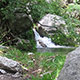 small waterfall cascading into spring surrounded by boulders and green vegetation