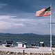 American flag flying adjacent to waterfront memorial with mountains in background