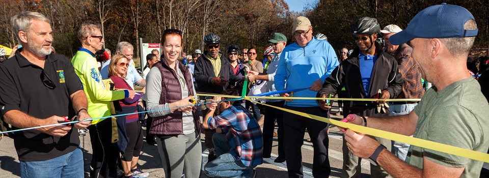 Group of men and women cutting ribbon on trail