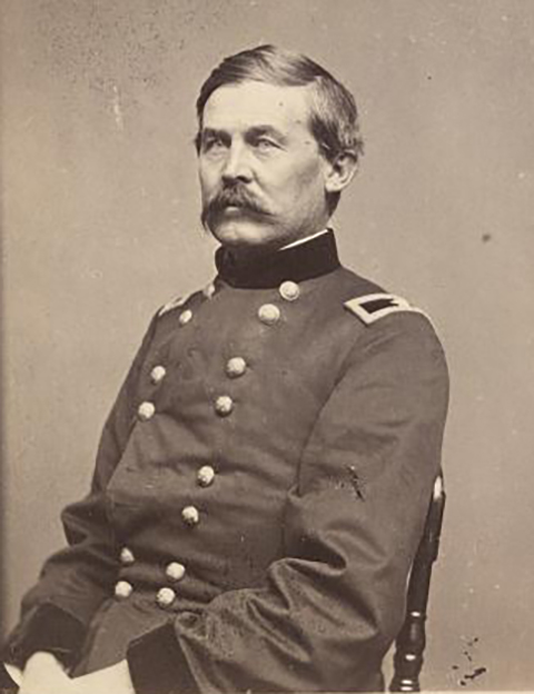 A black and white photo of a Union officer. He sits in a chair wearing his uniform. He has a mustache.