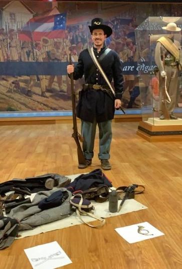An intern dressed in the uniform of a Civil War soldier with musket and soldier equipment