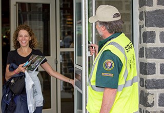 A park volunteer holds the door open for a park visitor.