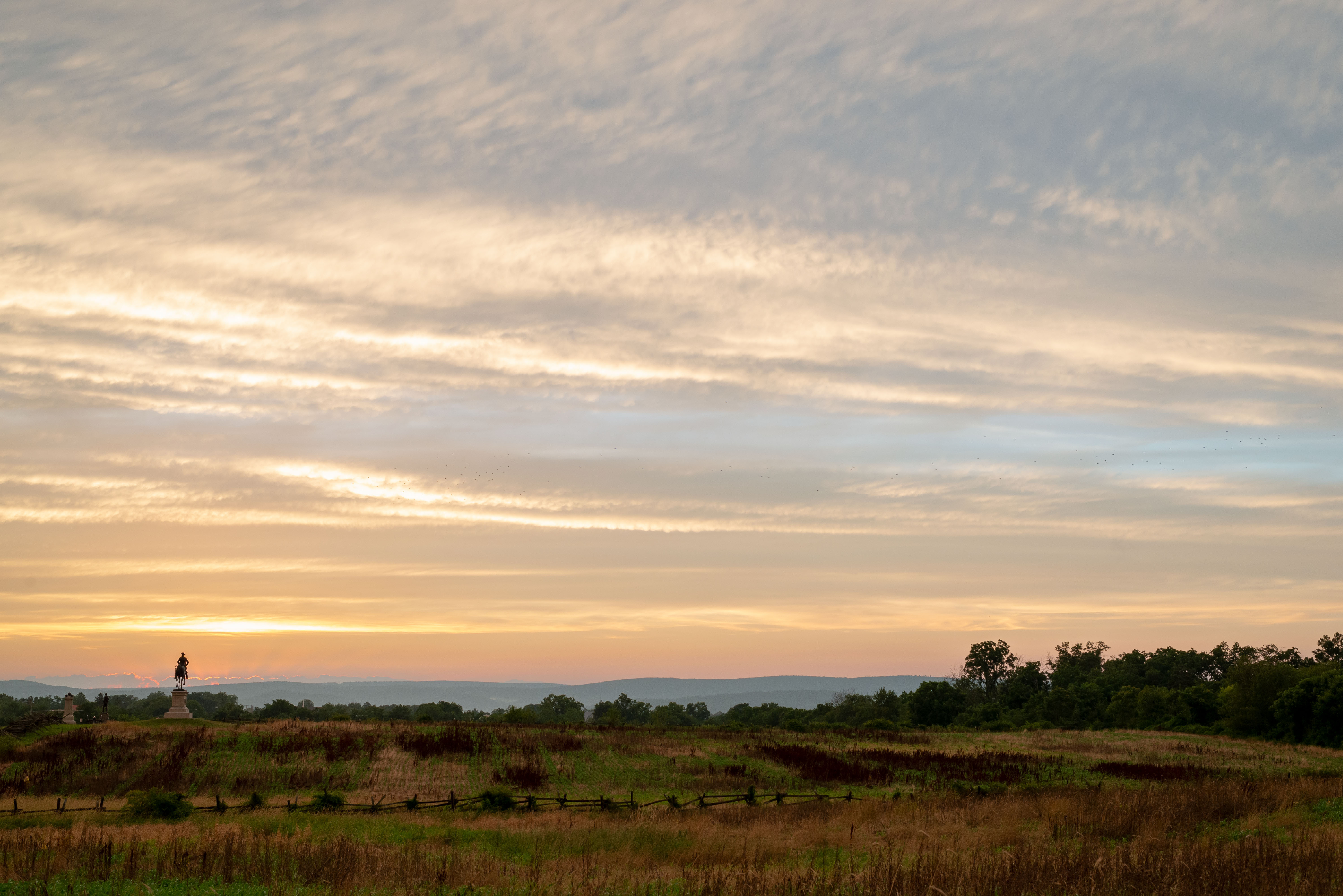 Farm fields with an equestrian statue in the distance silhouetted by the sunset.
