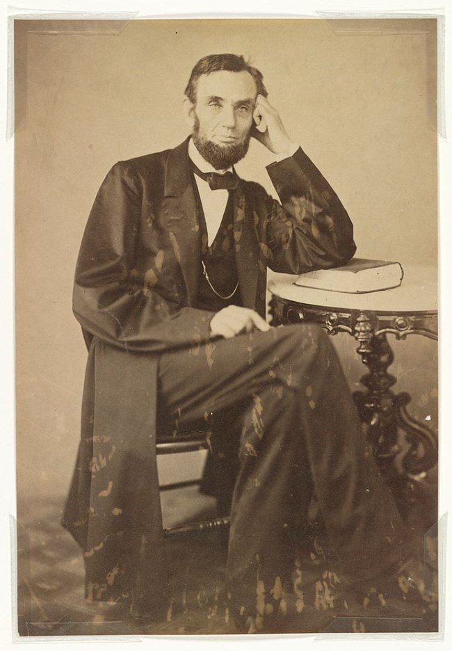 Abraham Lincoln by Gardner 1863 A photograph of a seated Abraham Lincoln at table with left hand held against his head, looking into camera.