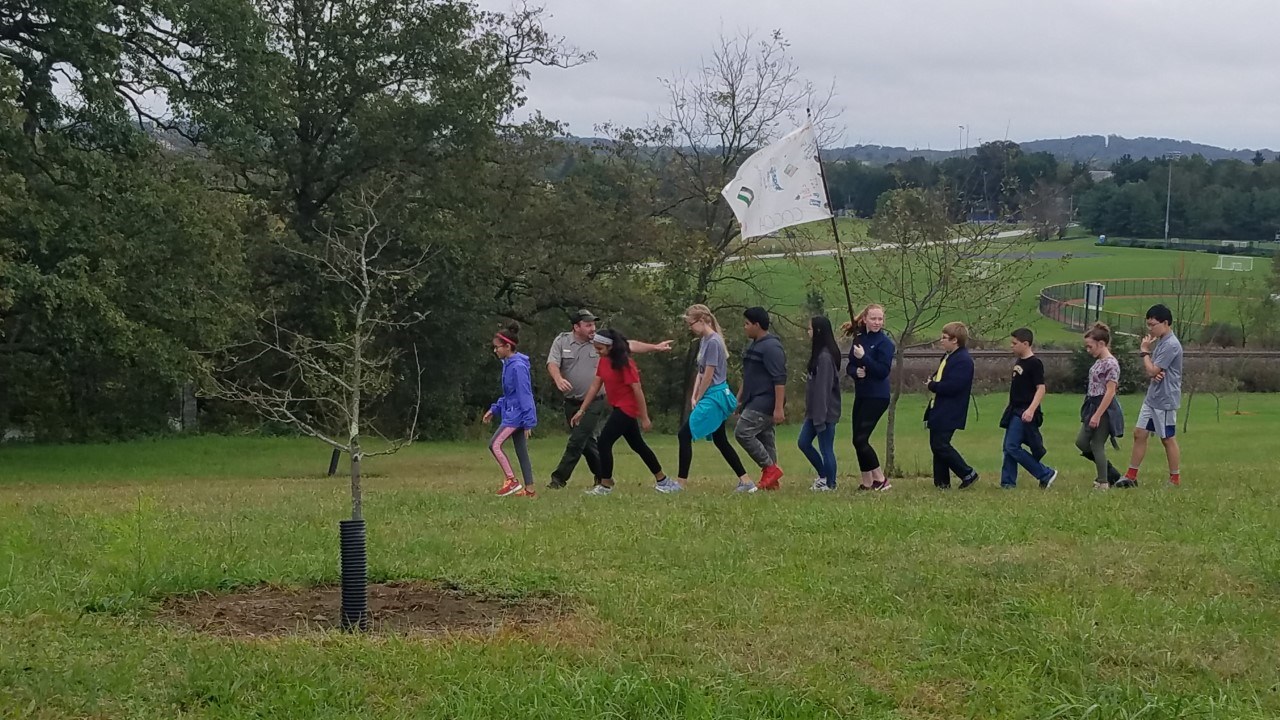 A Park Ranger leads a group of students, one of whom is carrying a flag.