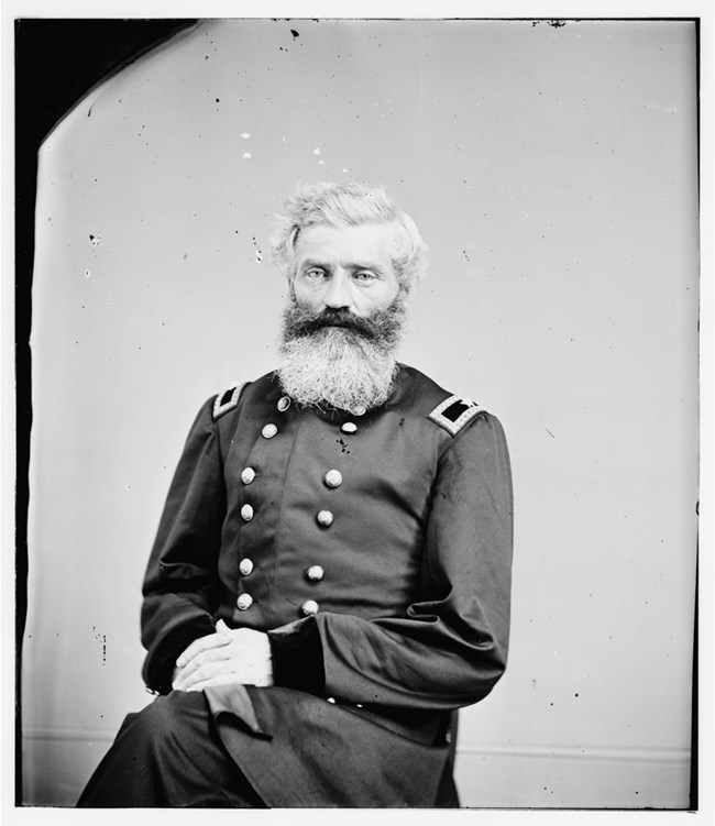 General Henry Baxter with a large white beard, sits for a photograph while wearing the uniform of a U.S. Civil War general