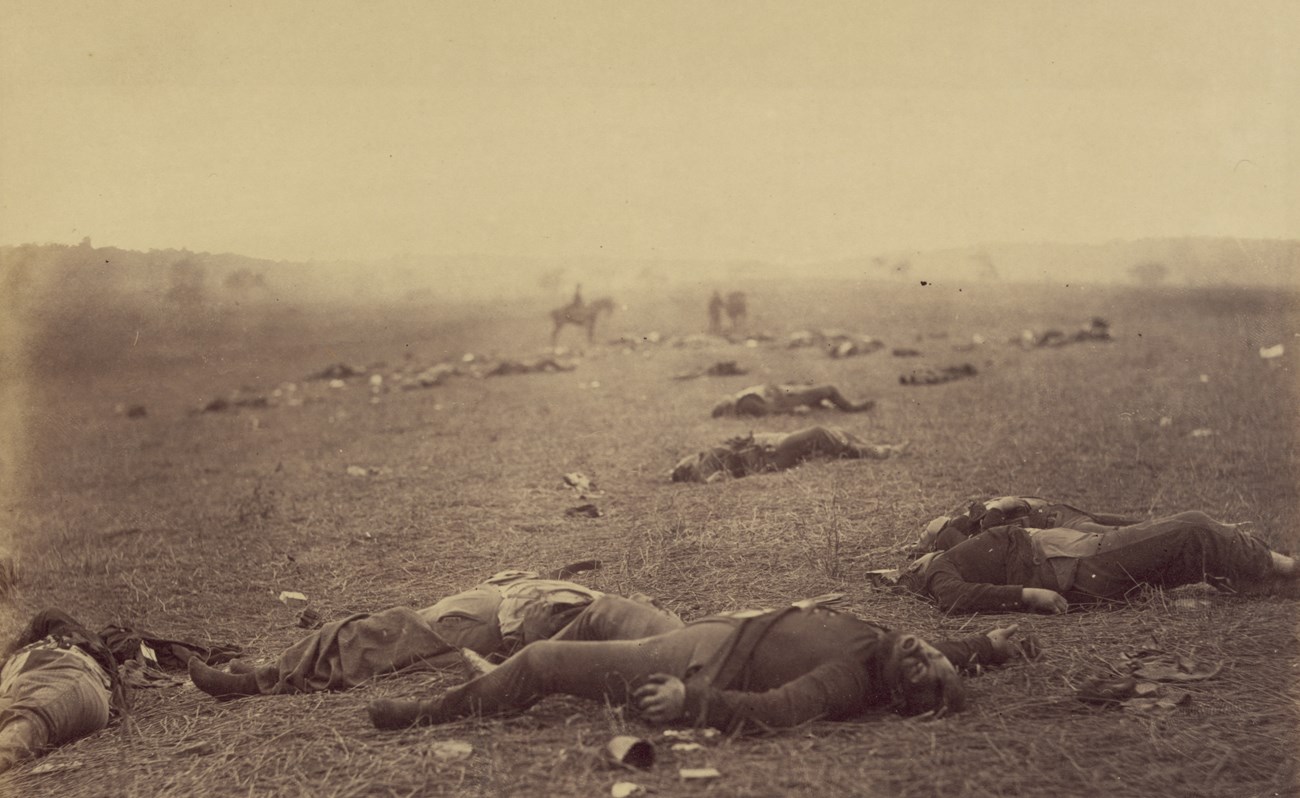 Historical black and white photograph of flat, open field with scattered dead bodies.