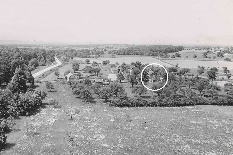 A black and white photo of the Warfield house along Seminary Ridge. It is nestled in a grove of trees from a distance.
