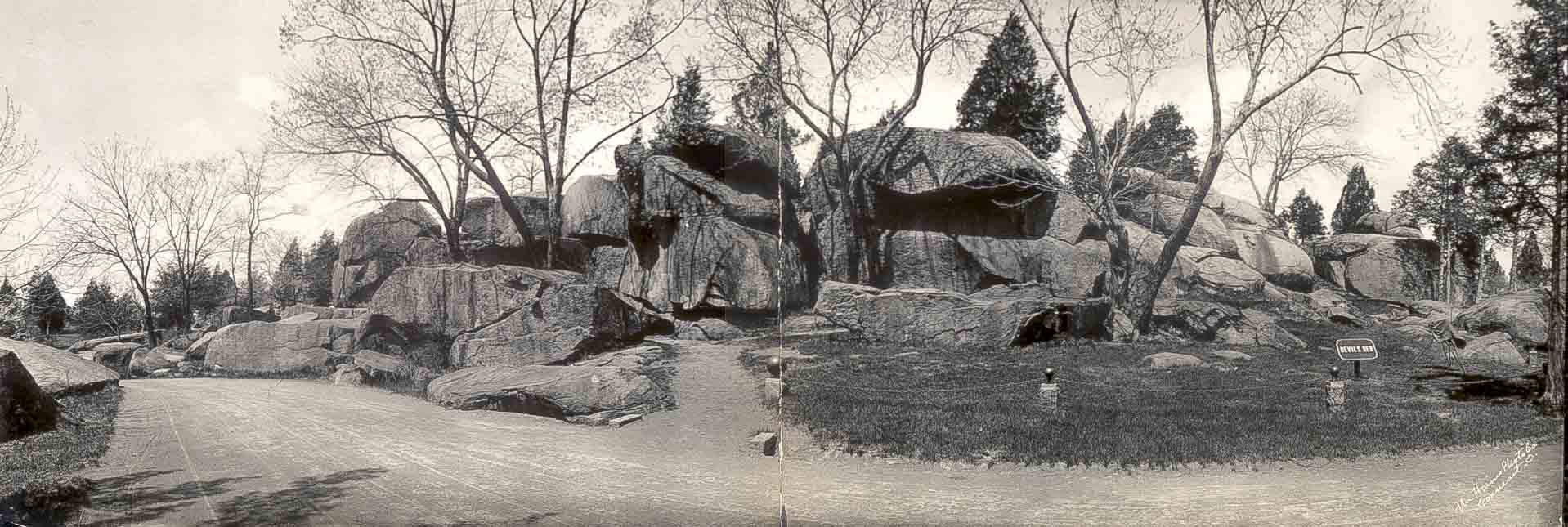 A black and white photograph of large boulders, many stacked on top of each other, with a few trees in the background.