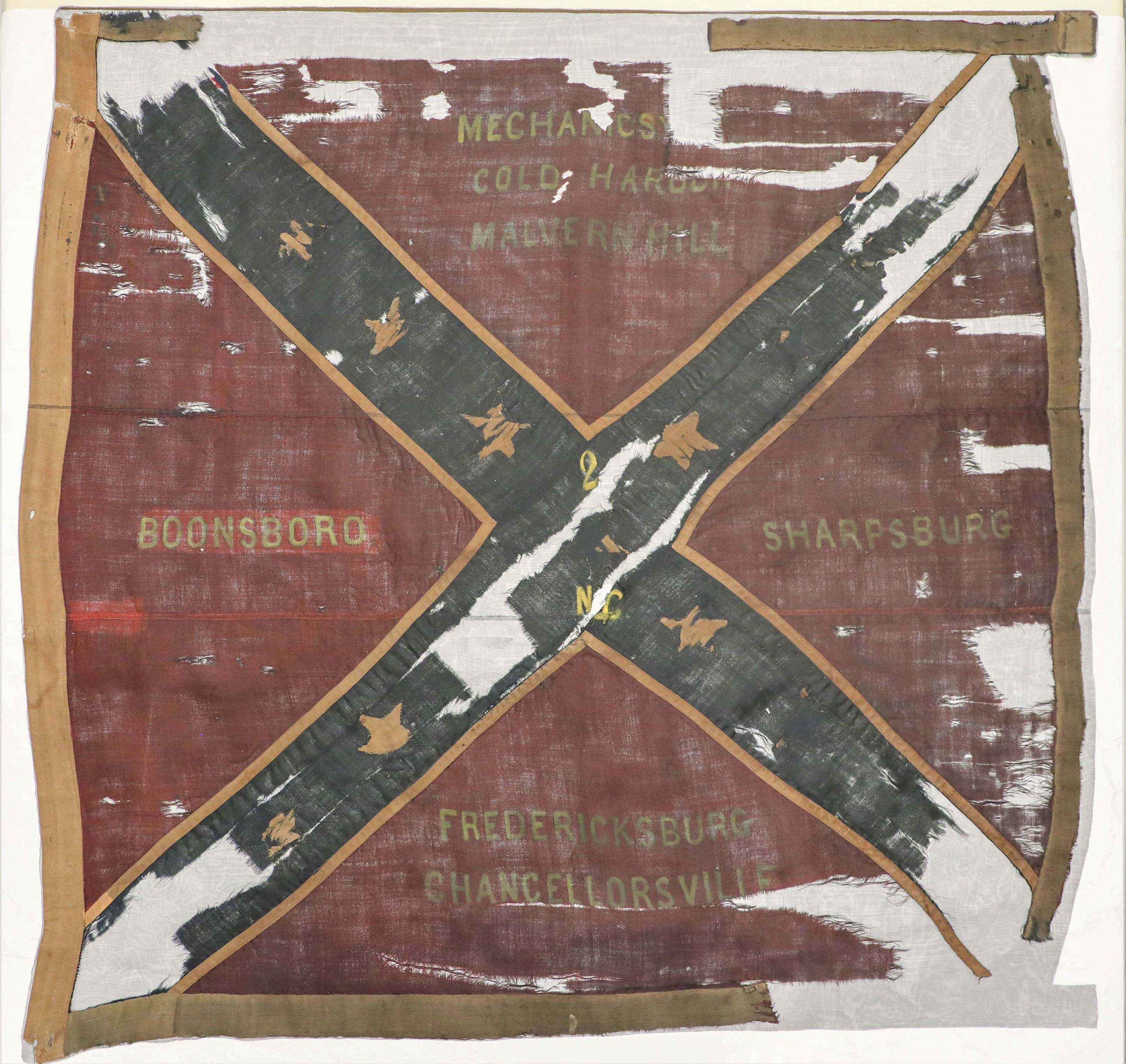 A tattered and worn red flag, with a blue X and small white stars inside the X. There are seven town names sewn into the red the red quadrants.