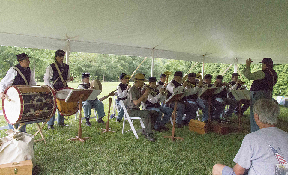 A Civil War band plays for a group of visitors under a large white tent.