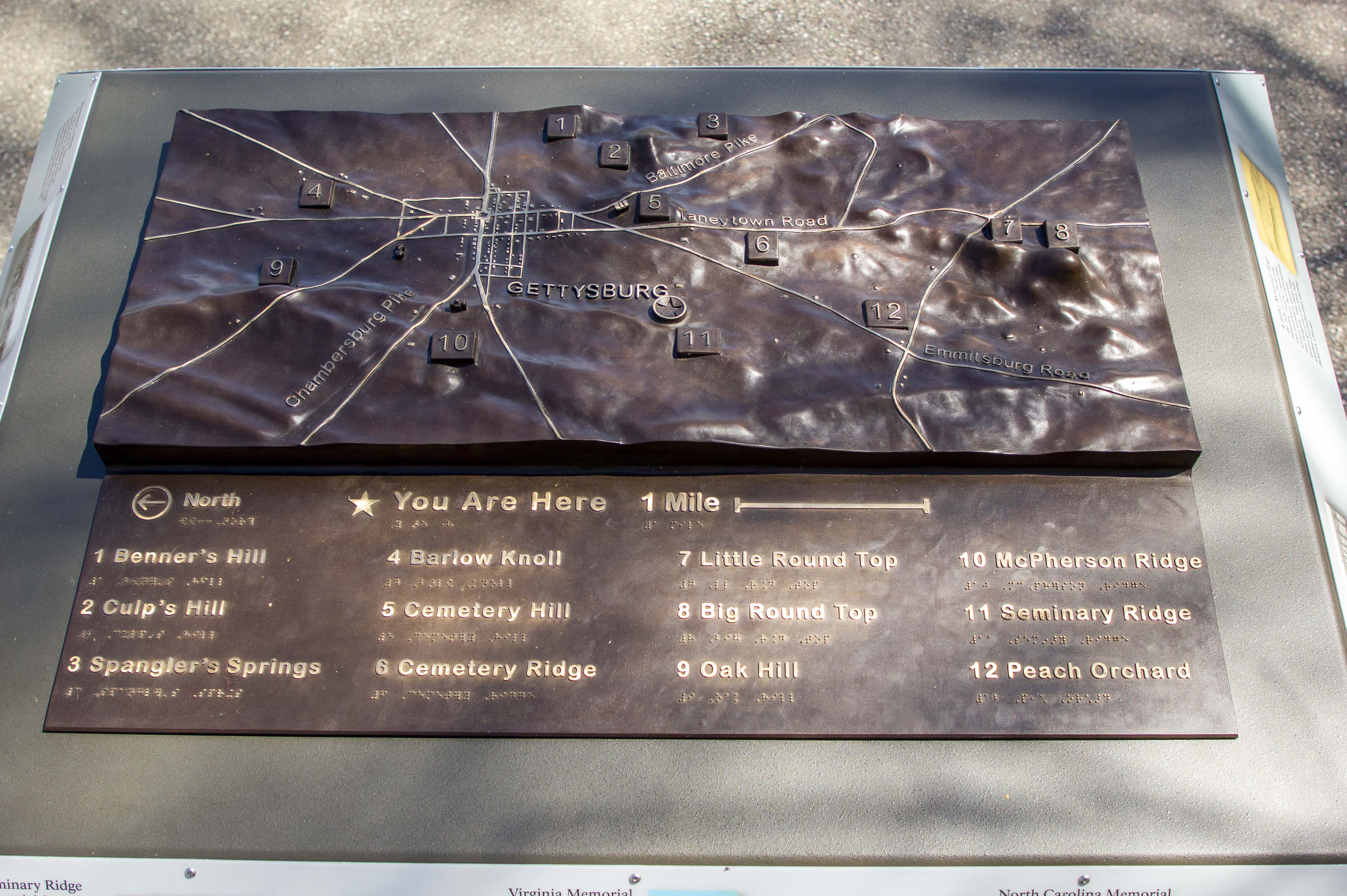 A bronze relief tactile map of the Gettysburg battlefield includes braille and raised lettering. A bronze relief tactile map of the Gettysburg battlefield includes braille and raised lettering.