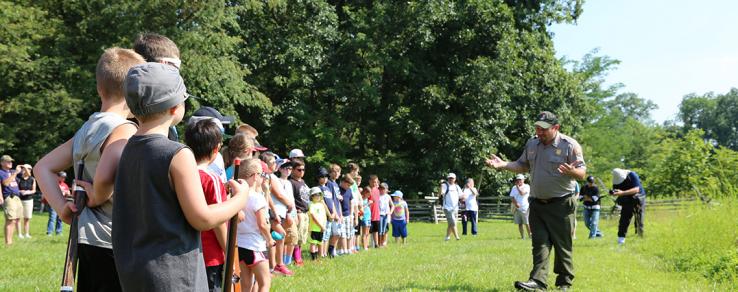 A park ranger discusses the Battle of Gettysburg with a large group of children.