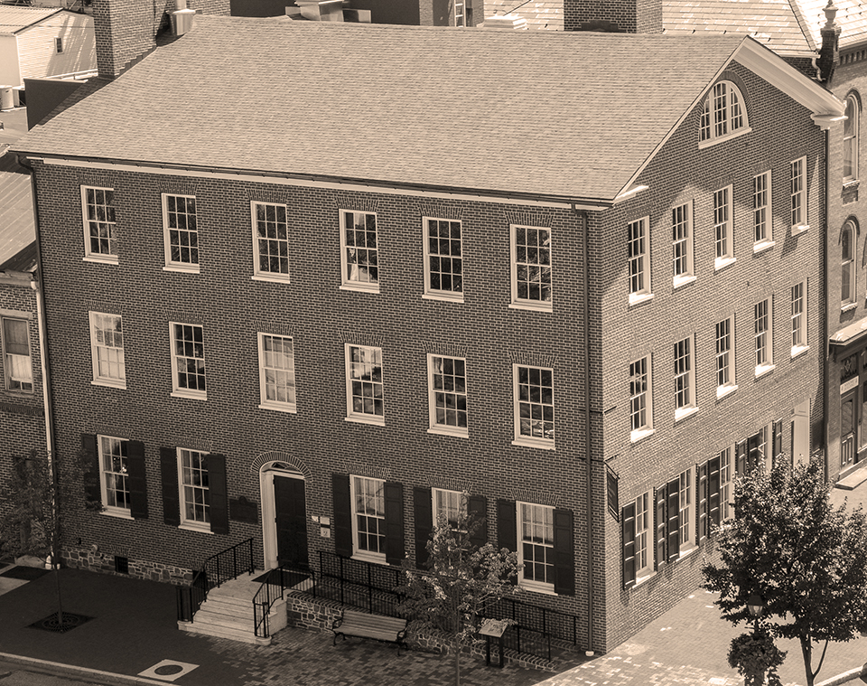A photograph of the Wills house in the center of Gettysburg. The building is a three story, red brick home but the photo has had a sepia tone filter applied to it.