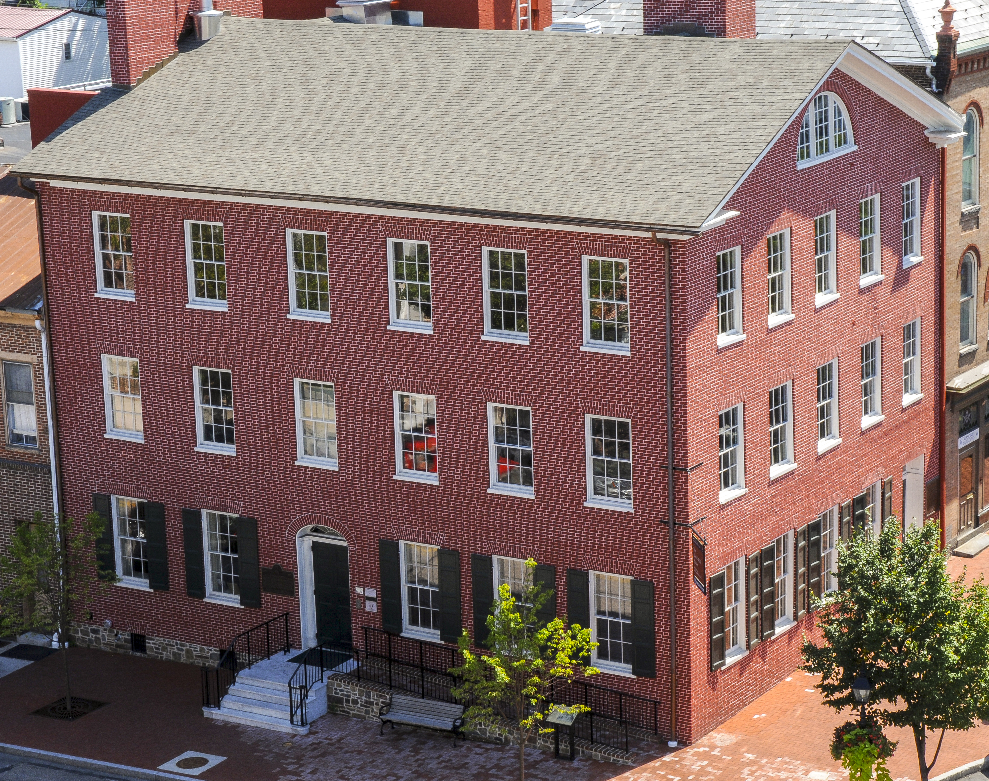 A three-story red brick house as seen from above. There are red brick sidewalks on two sides of the house.