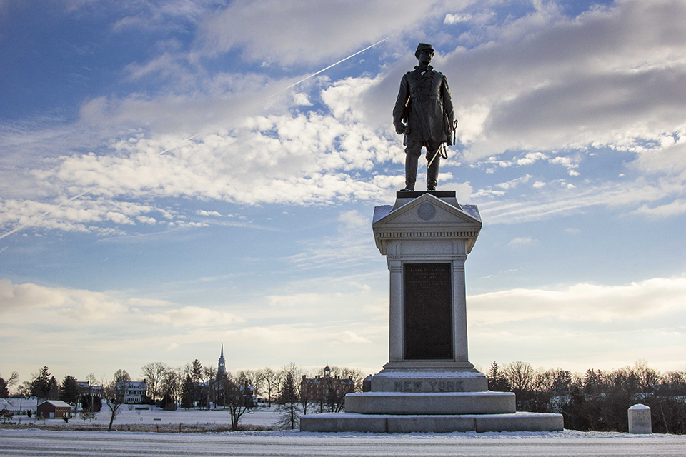 The Abner Doubleday monument with buildings in the background and fresh snow on the ground.