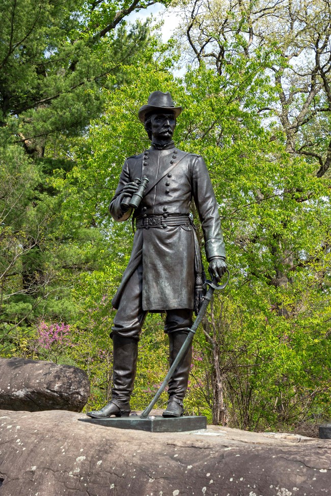 A bronze statue of a soldier holding binoculars ontop of a boulder