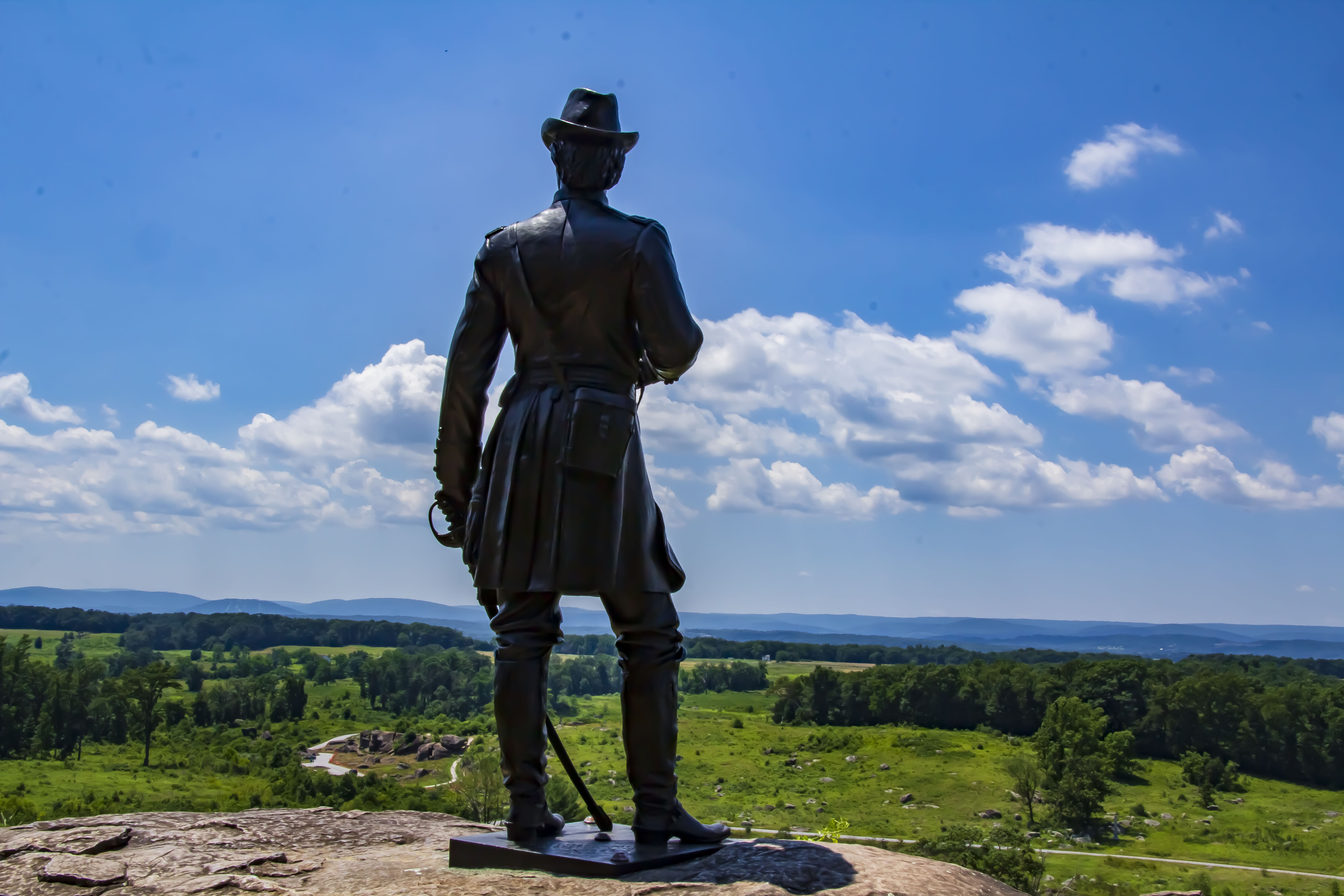 A Statue stands ontop of a boulder looking over a hill into the distance