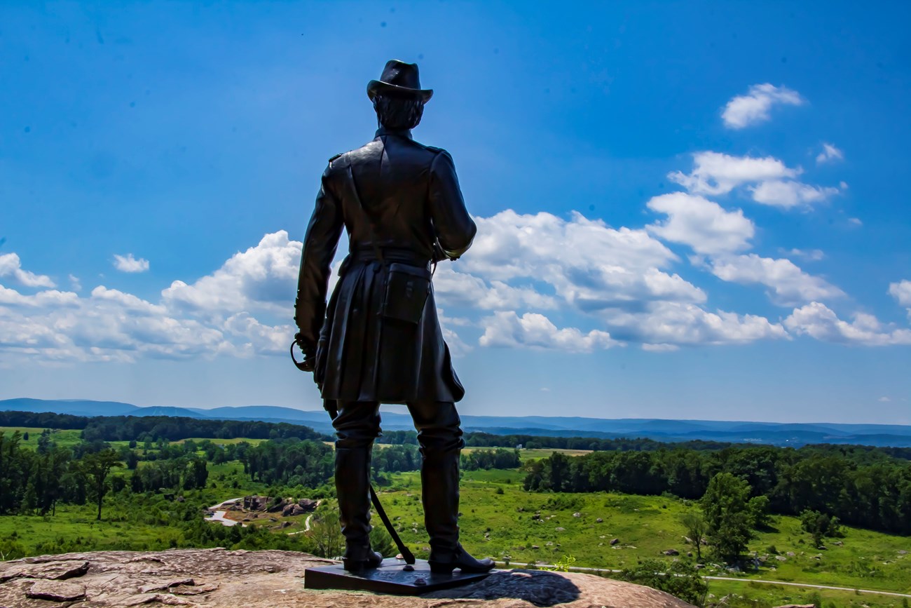 A Statue stands ontop of a boulder looking over a hill into the distance